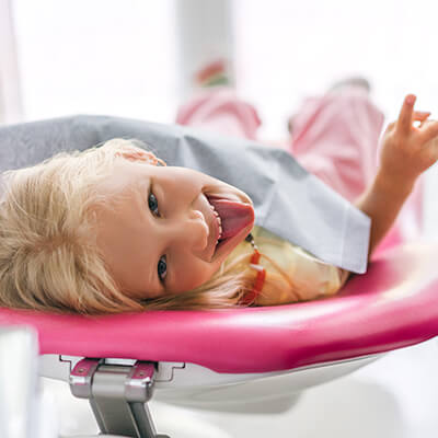 A girl lying in the dentist's chair while smiling and sticking out her tongue