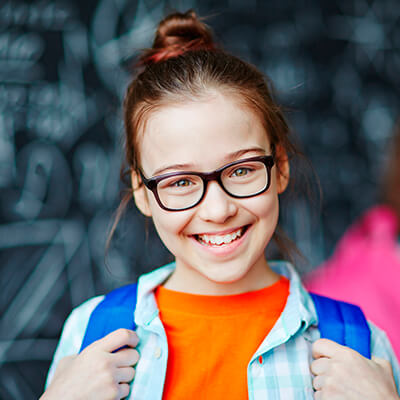 A girl with glasses smiling in front while standing with a blue backpack