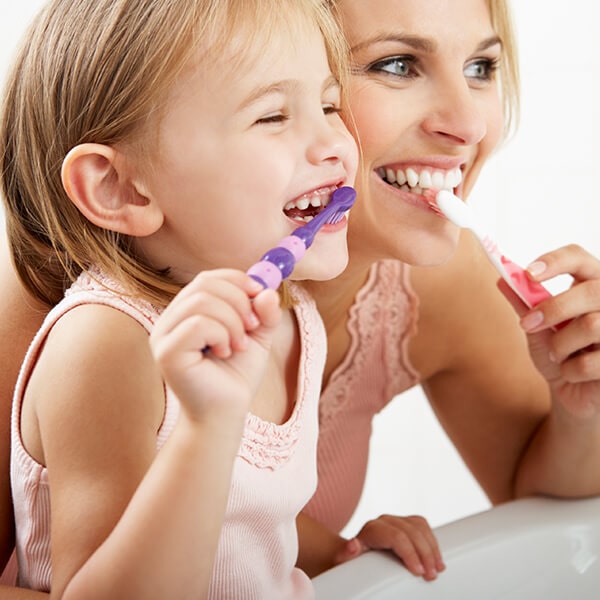 A mother brushing her teeth with her little daughter while they smile and look in the mirror