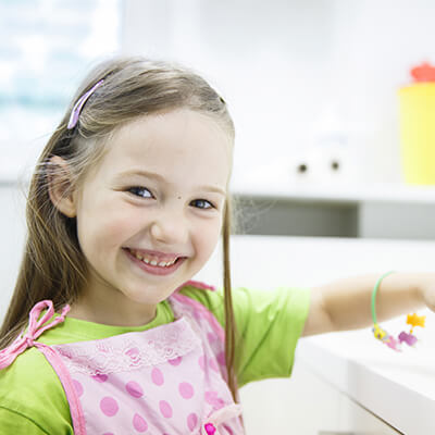 A girl in the kitchen wearing a pink apron while smiling