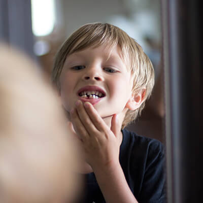 A boy looking at his teeth in front of the mirror after getting one of our dental services