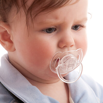 A little boy wearing a pacifier while looking down 