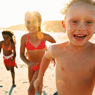 Three children running on the beach while the sun covers them
