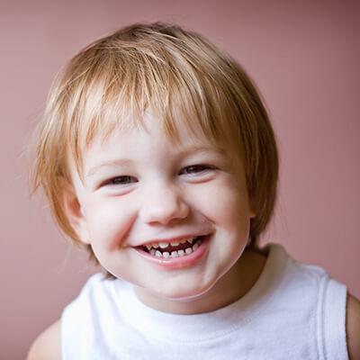 A boy who has experienced our dental services smiling in front of a pink background